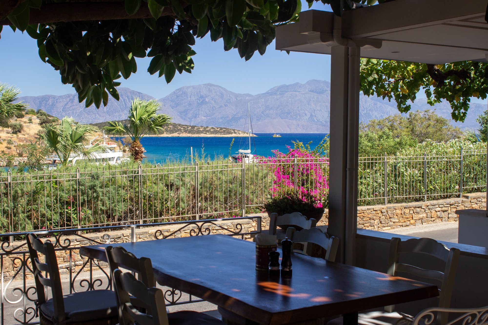 The terrace at Kri Kri under the pergola, tables set with the bay of Órmos behind